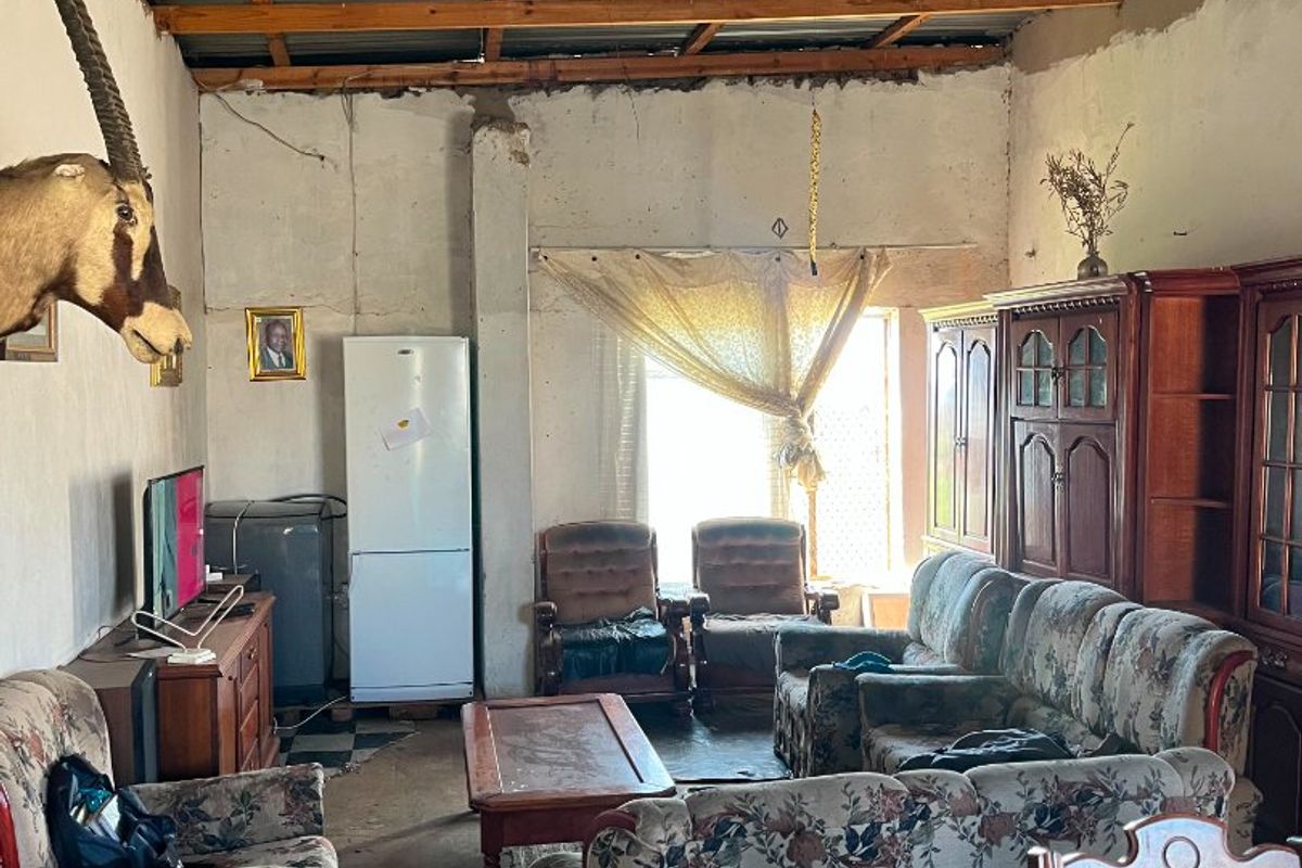 A rustic living area featuring exposed timber roof trusses, corrugated metal ceiling, and concrete flooring, requiring significant renovation to improve finishes and structural presentation.