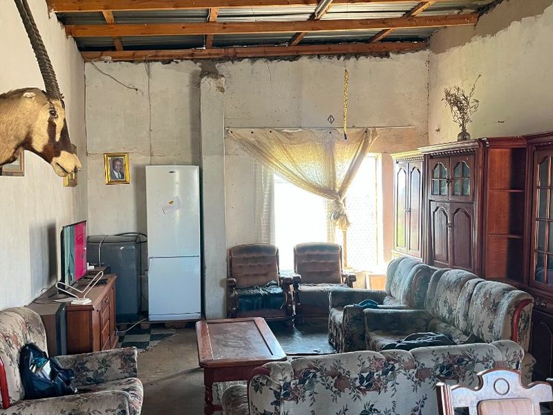 A rustic living area featuring exposed timber roof trusses, corrugated metal ceiling, and concrete flooring, requiring significant renovation to improve finishes and structural presentation.