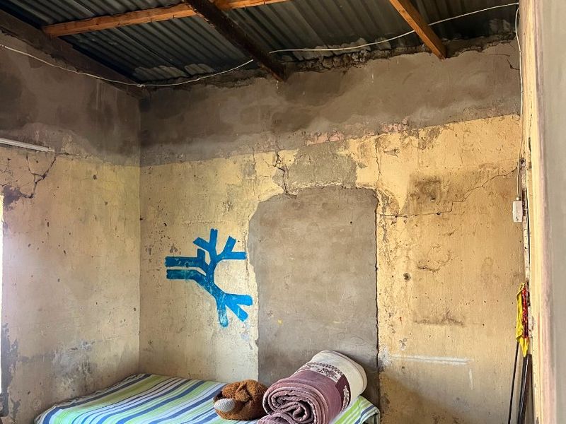 A bedroom space featuring exposed timber rafters and corrugated iron roofing, requiring significant renovation to the walls and flooring to improve its condition.