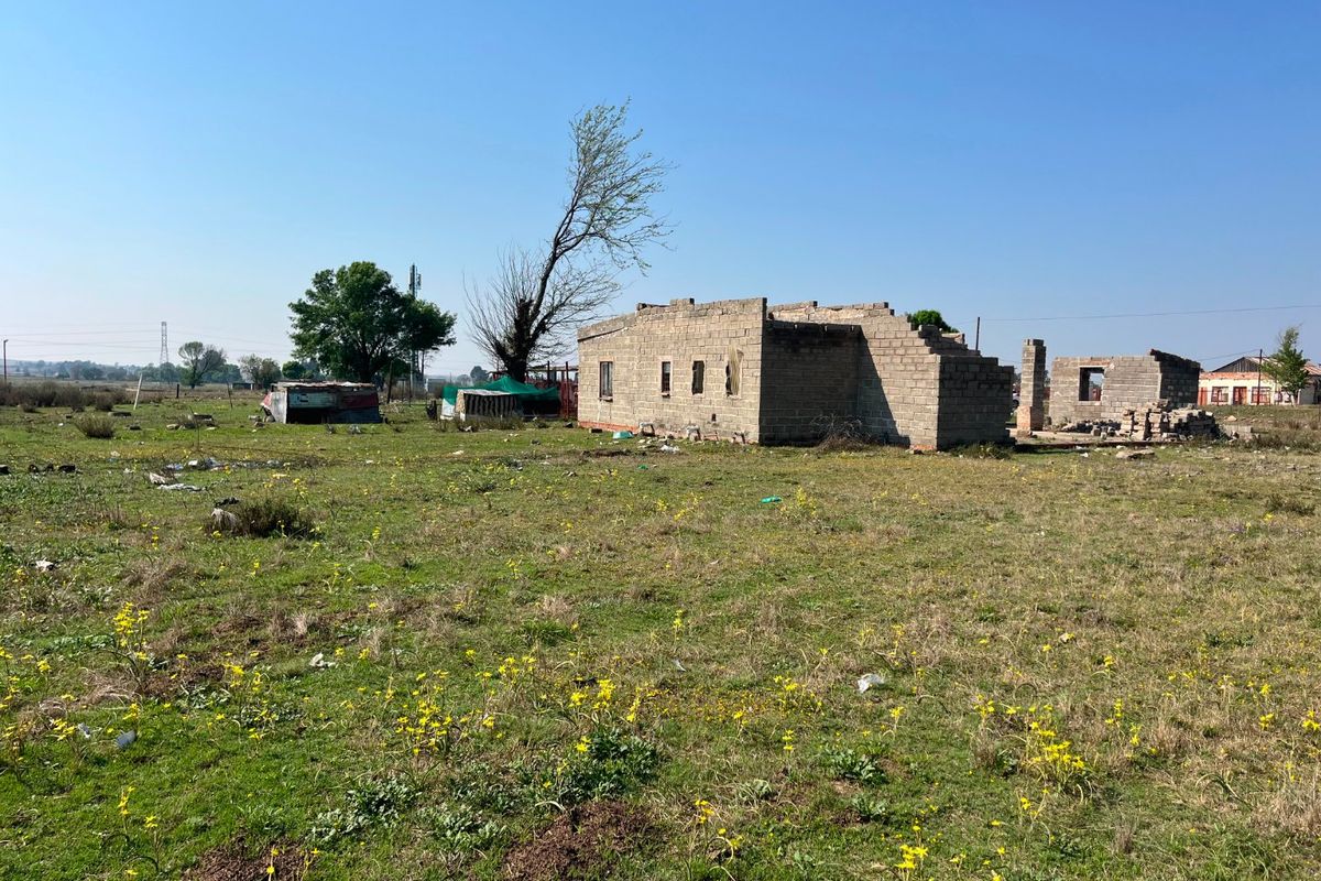 An unfinished concrete block structure on a large rural farm plot, currently in the early stages of construction.