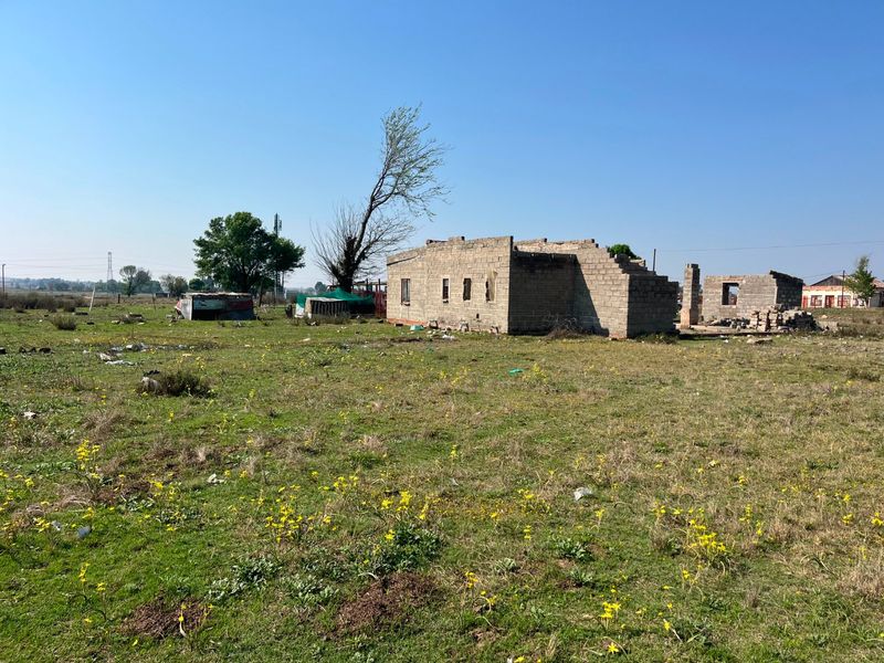 An unfinished concrete block structure on a large rural farm plot, currently in the early stages of construction.