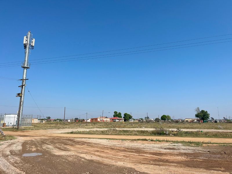 A wide-angle view of a rural property featuring a prominent telecommunications tower, dirt access road, and surrounding open land.