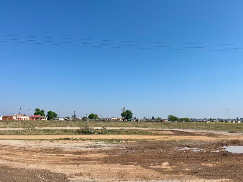 A wide-angle view of an undeveloped plot of land with an unpaved access road in the foreground and distant rural structures.