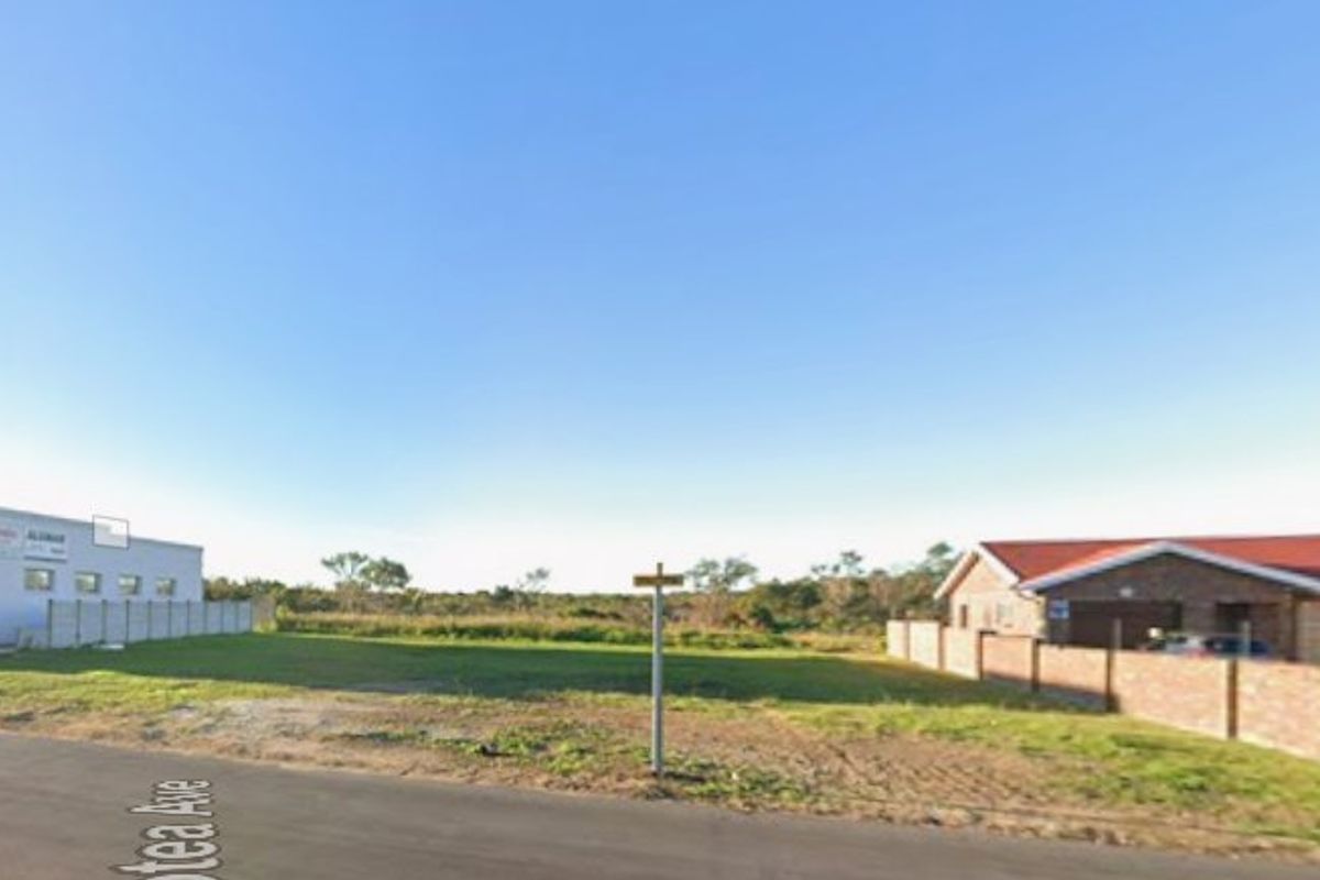 A street-level view of a vacant residential plot situated between existing properties, featuring boundary walls and direct road access.