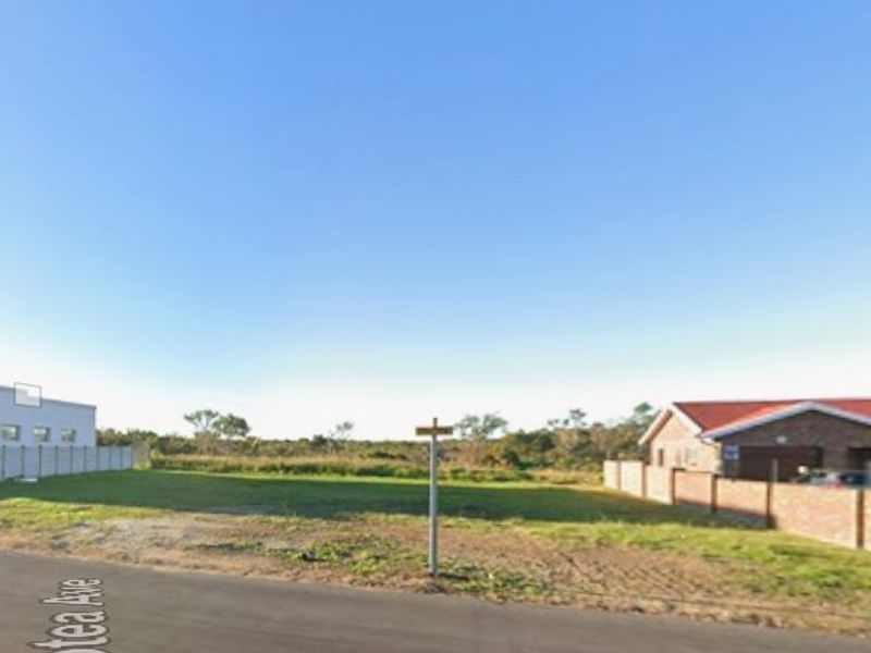 A street-level view of a vacant residential plot situated between existing properties, featuring boundary walls and direct road access.