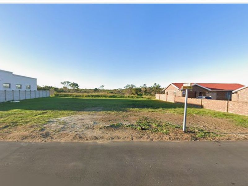 A vacant residential plot of land situated between existing properties, featuring a boundary wall and direct access to a paved street.