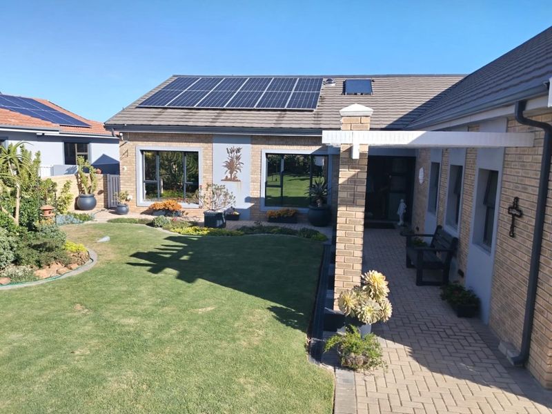 A well-maintained rear exterior featuring a brick facade, solar panels, a paved patio area, and a neatly landscaped garden.
