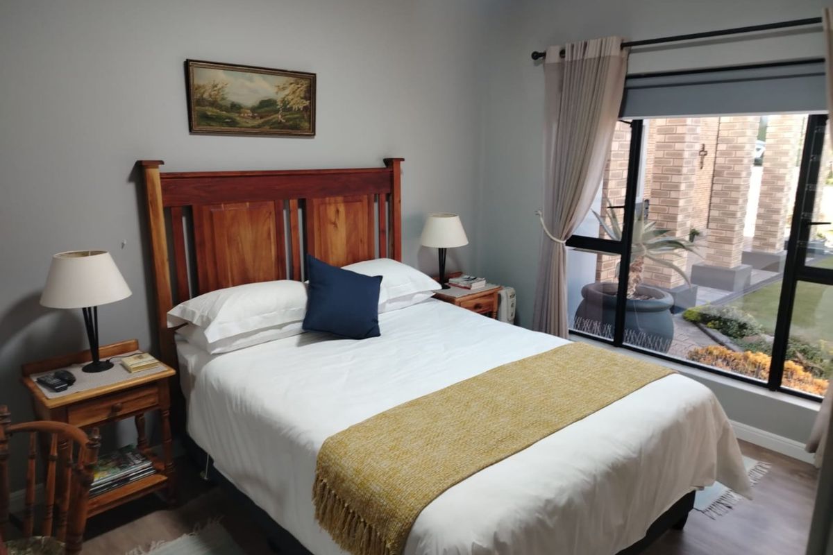 A well-maintained bedroom featuring laminate flooring, neutral wall tones, and a large window providing natural light and views of the exterior garden area.