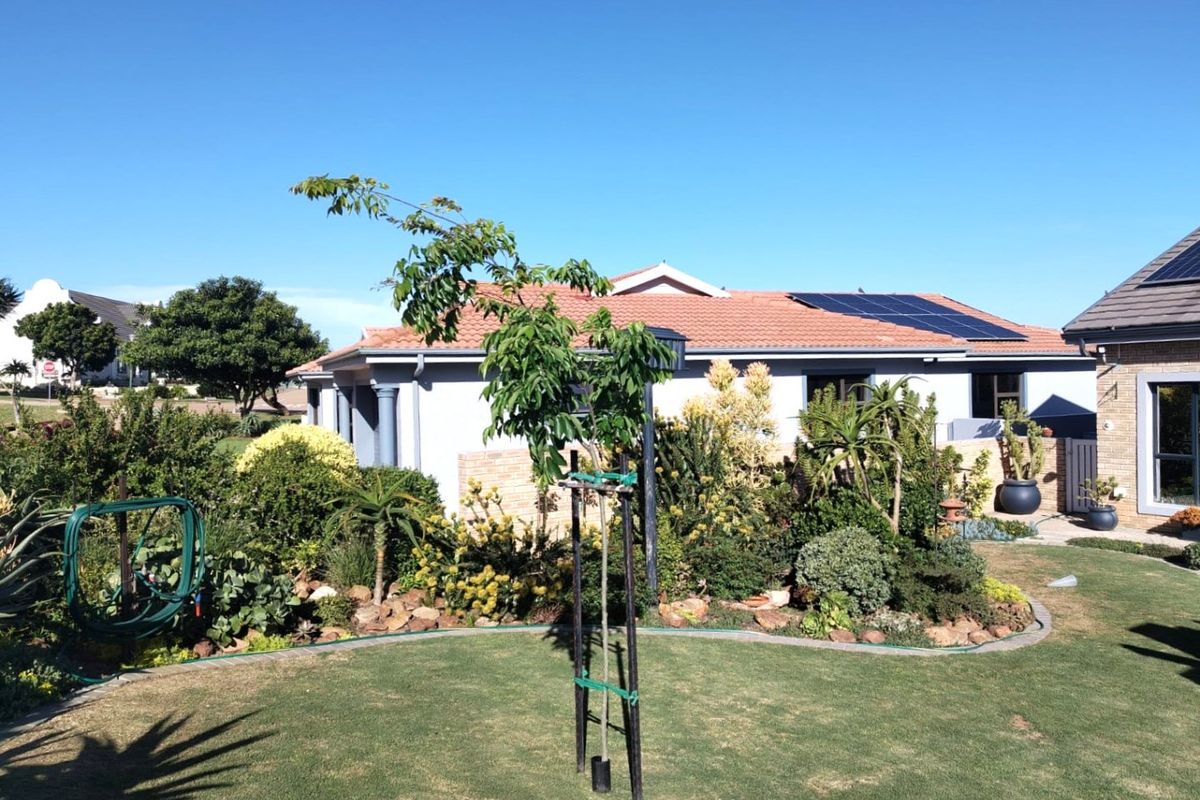 A well-maintained rear garden featuring a manicured lawn, established landscaping, and a house exterior equipped with roof-mounted solar panels.