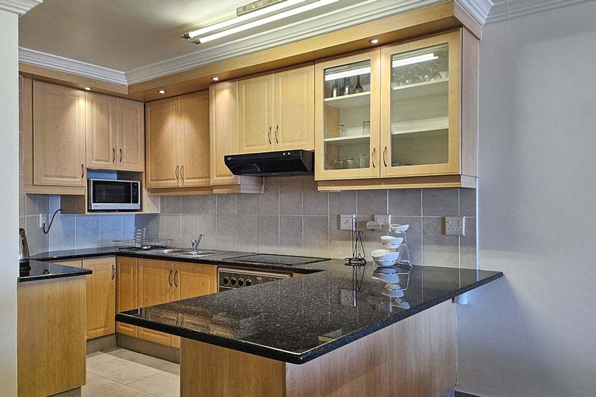 A functional kitchen featuring light wood cabinetry, dark granite countertops, a tiled backsplash, and integrated appliances including an oven, hob, and microwave.