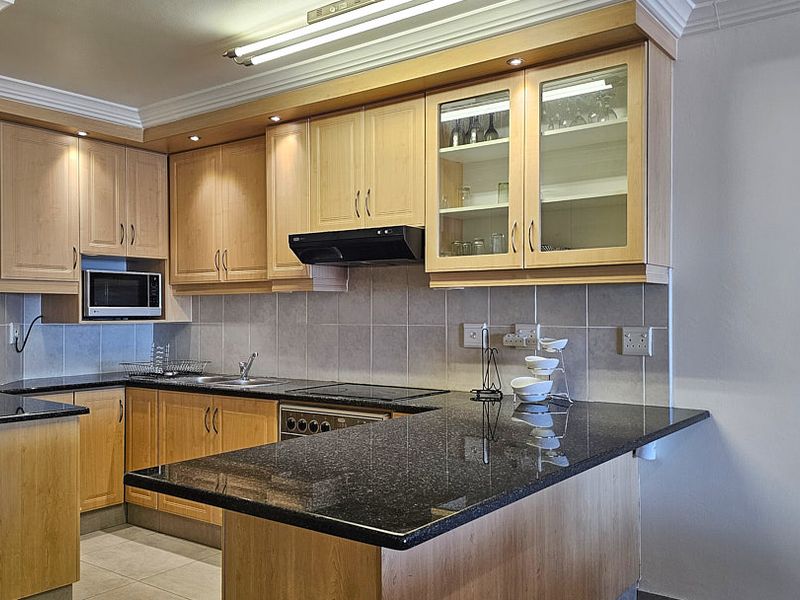 A functional kitchen featuring light wood cabinetry, dark granite countertops, a tiled backsplash, and integrated appliances including an oven, hob, and microwave.