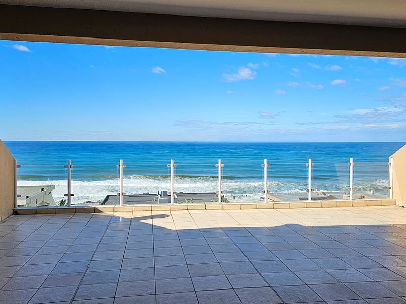 Spacious covered balcony featuring a glass balustrade and panoramic ocean views, providing an ideal outdoor space for relaxation.