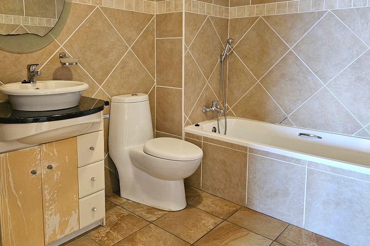 A bathroom featuring a tiled bathtub, toilet, and vanity cabinet with a vessel sink. The vanity cabinet shows signs of surface finish wear.