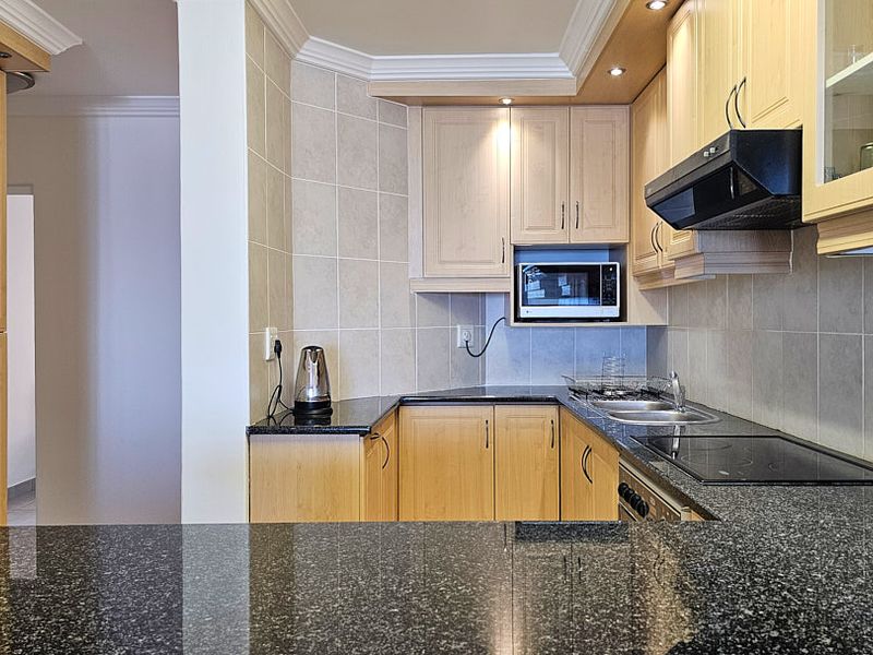 A functional kitchen featuring light wood cabinetry, dark granite countertops, a built-in hob, extractor fan, and a tiled backsplash.