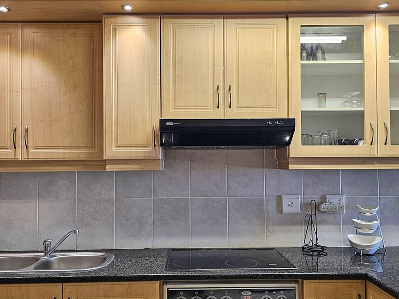 A functional kitchen featuring light wood cabinetry, granite countertops, a stainless steel double sink, and a built-in electric hob with an extractor fan.