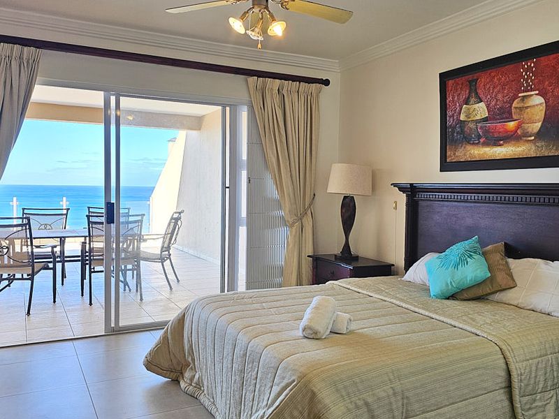 Spacious bedroom featuring tiled flooring, crown molding, and a large sliding glass door providing direct access to a private balcony with ocean views.