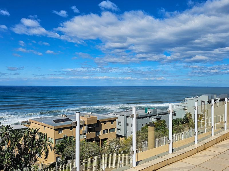 Spacious balcony featuring tiled flooring, a glass balustrade, and an outdoor chimney, offering expansive ocean views.