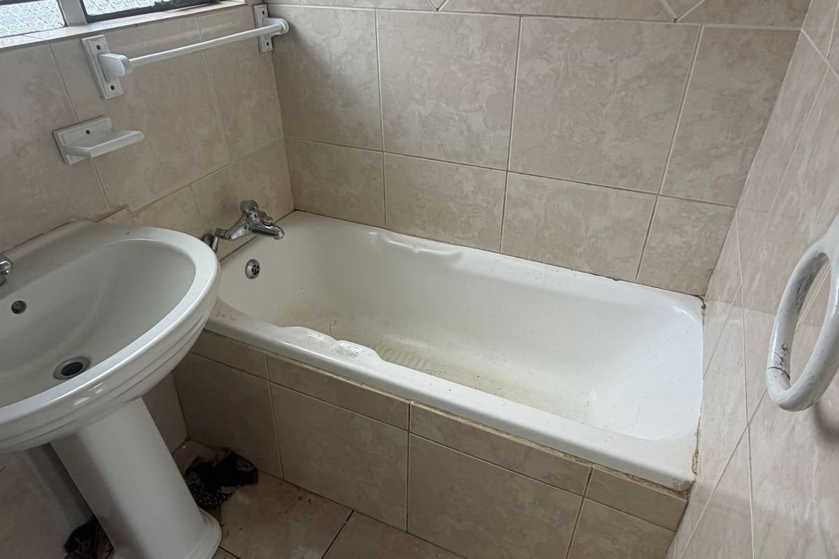 A dated bathroom featuring a pedestal basin and a built-in bathtub with tiled surrounds, requiring cosmetic updates to improve its condition.