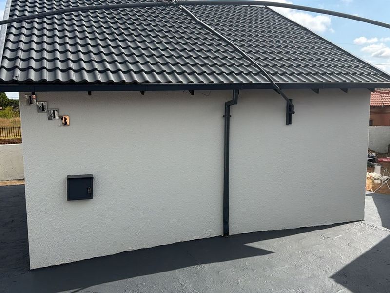 Exterior view of a townhouse featuring a clean tiled roof, painted concrete driveway, and wall-mounted mailbox.