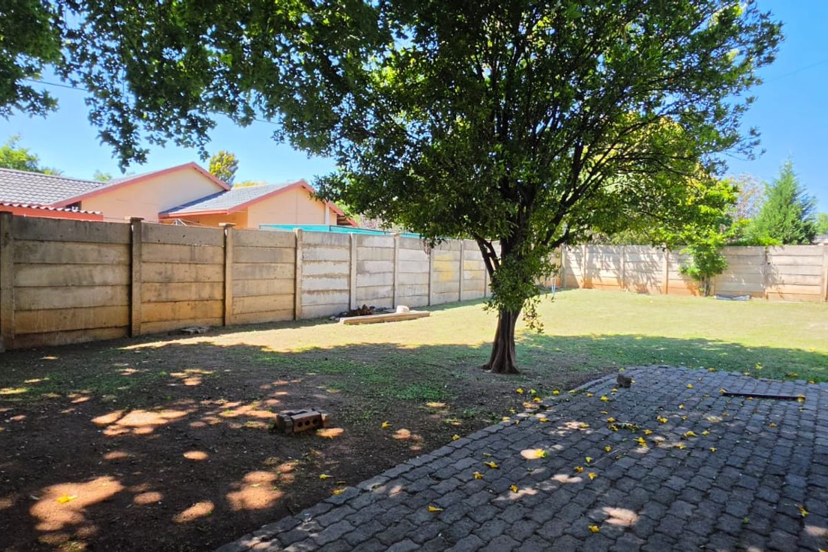 A spacious rear garden featuring a paved patio area, established tree, and secure precast concrete boundary walls.