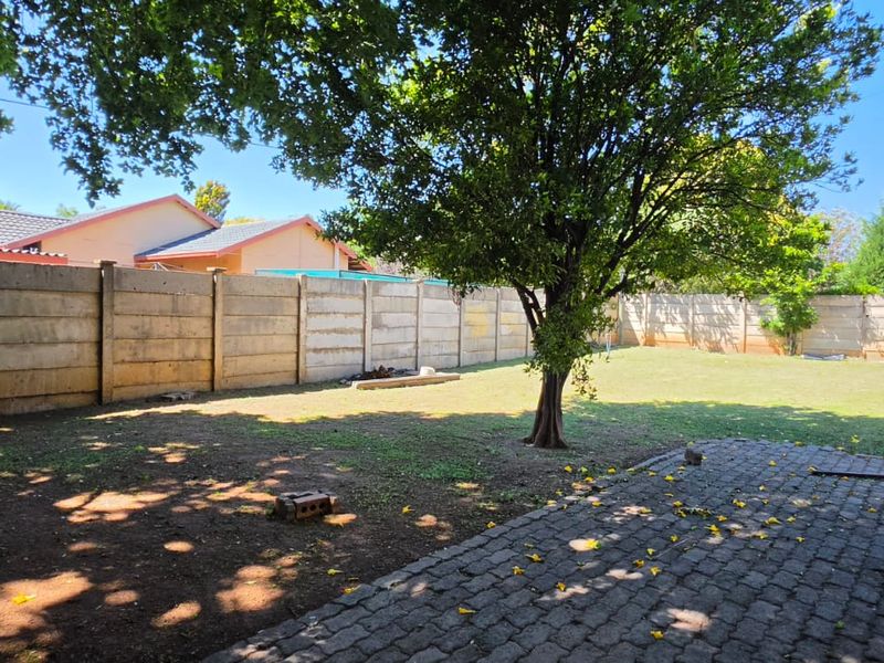 A spacious rear garden featuring a paved patio area, established tree, and secure precast concrete boundary walls.