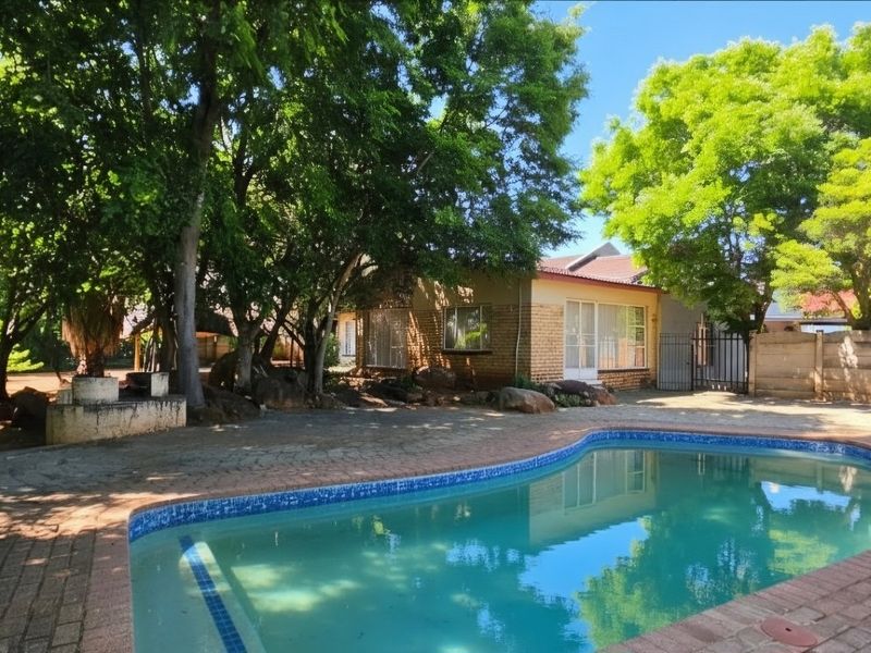 A private backyard featuring a swimming pool with brick paving, mature trees, and a secure boundary wall.