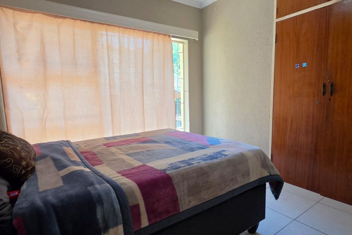 A functional bedroom featuring tiled flooring, a built-in wooden wardrobe, and a window with security bars, offering a neutral base for updates.