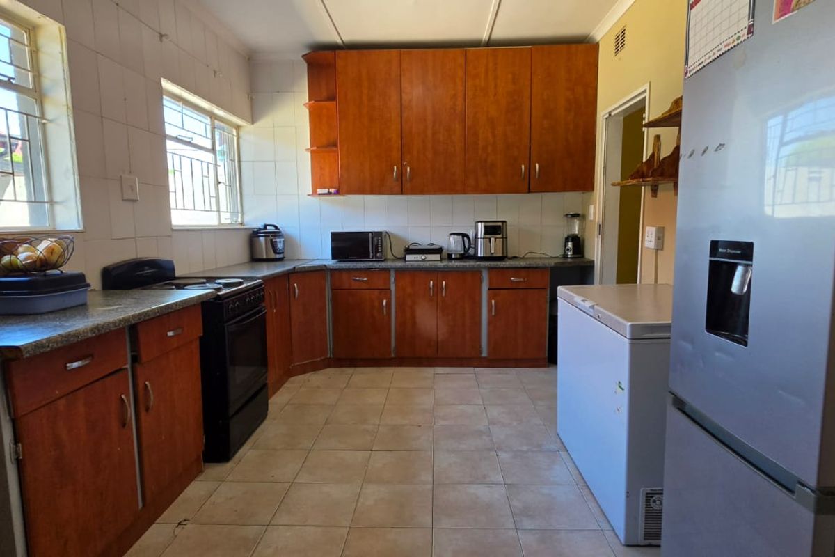 A functional kitchen featuring wooden cabinetry, stone countertops, tiled flooring, and a tiled backsplash, with security bars installed on the windows.