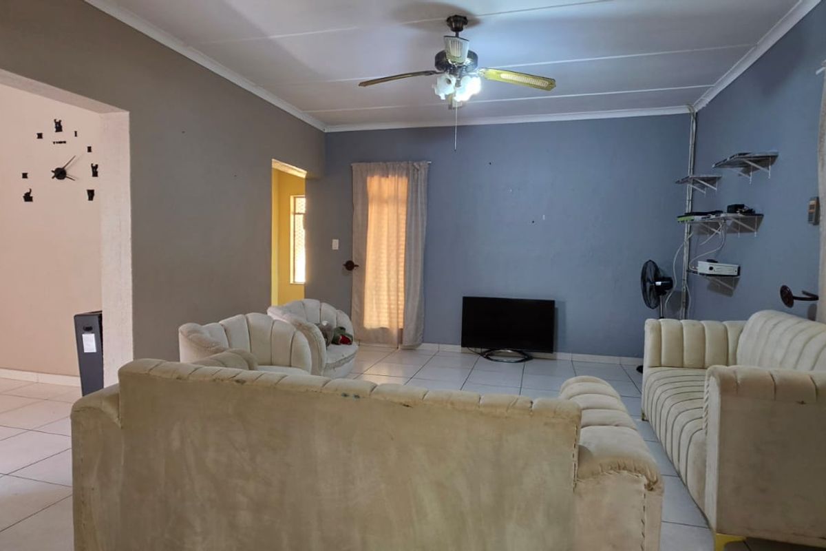 A spacious living room featuring tiled flooring, a ceiling fan, and neutral wall tones, offering a functional layout for comfortable family living.
