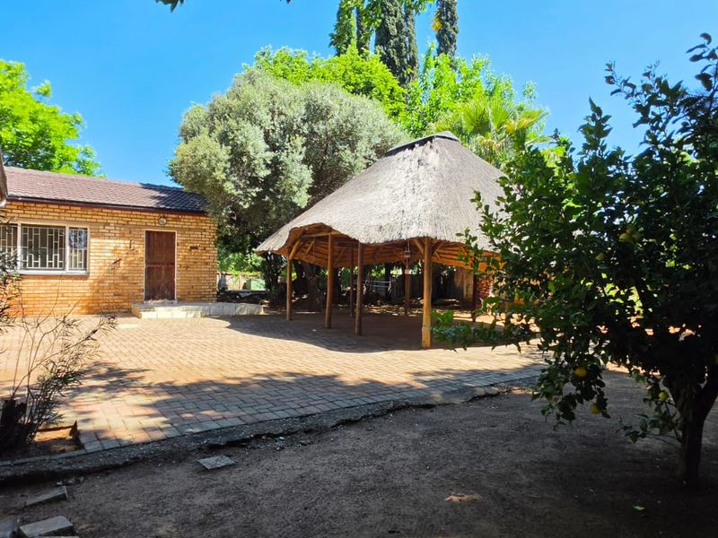 Rear garden area featuring a traditional thatched lapa, brick paved patio, and a detached brick outbuilding.