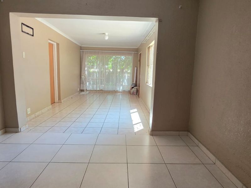 An empty, open-plan living area featuring tiled flooring and a sliding glass door leading to the exterior.