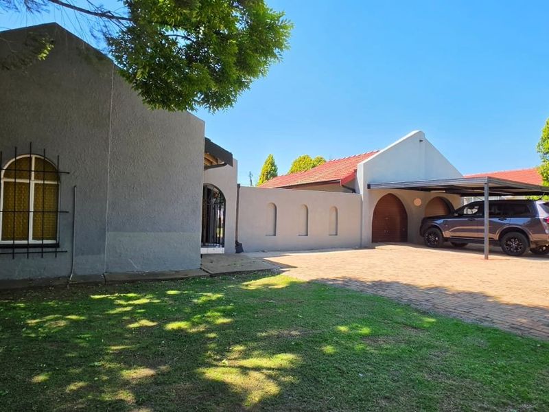 Front exterior view of the house featuring a paved driveway, carport, and a well-maintained garden area.