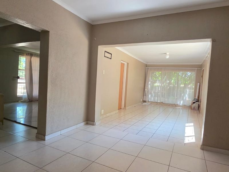 Spacious open-plan living area featuring neutral tiled flooring and large windows, offering a versatile layout ready for modern updates.