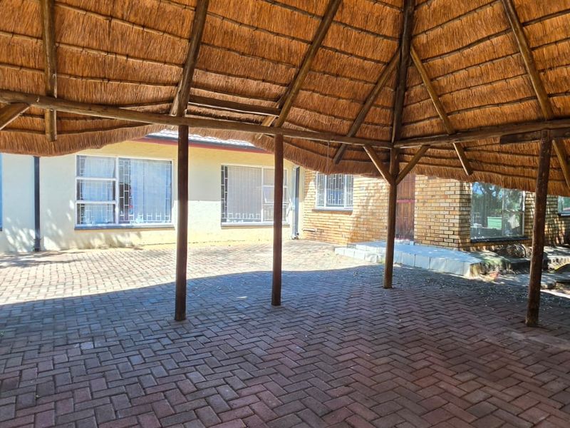A covered outdoor patio area featuring a traditional thatch roof, timber support structure, and brick paving, providing a shaded space for outdoor relaxation.