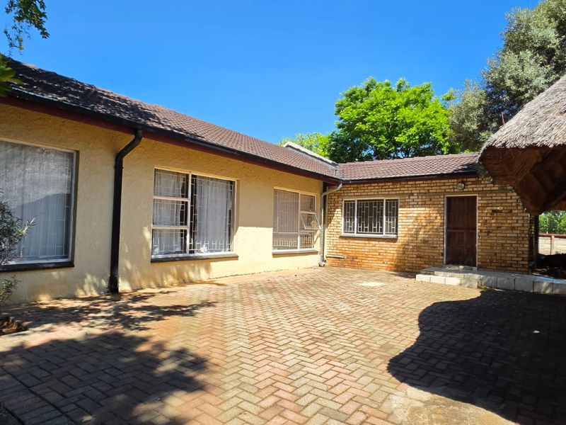 Rear exterior view featuring a paved courtyard, brick and plastered wall finishes, and a traditional thatched lapa structure.