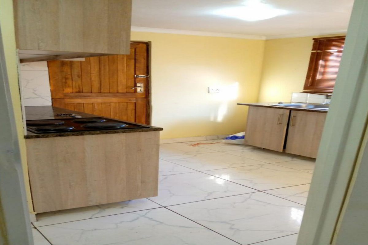 A functional kitchen featuring light wood-finish cabinetry, dark countertops, an integrated hob, and tiled flooring, offering a clean and practical workspace.