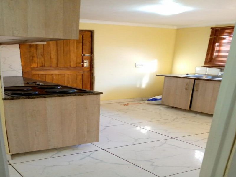A functional kitchen featuring light wood-finish cabinetry, dark countertops, an integrated hob, and tiled flooring, offering a clean and practical workspace.