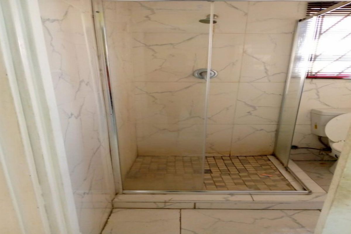 A functional bathroom featuring a glass-enclosed shower with tiled walls and flooring, alongside a standard toilet.