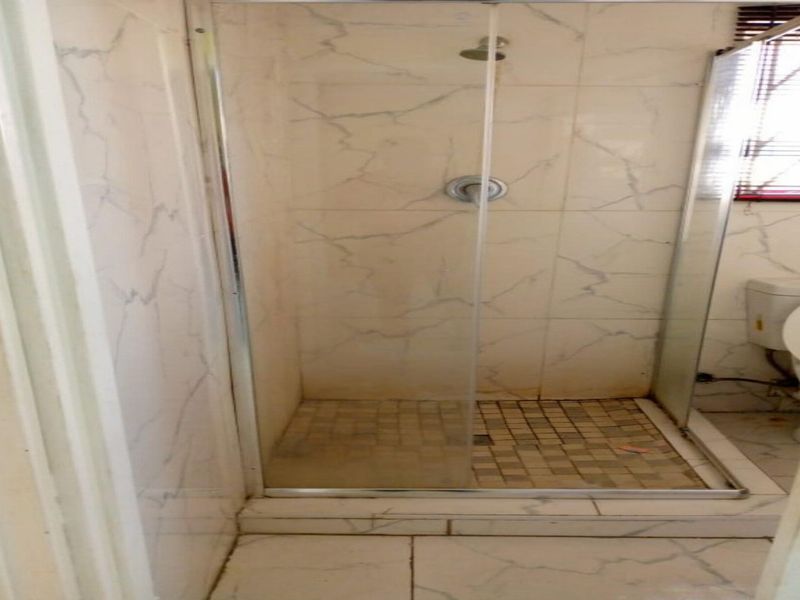 A functional bathroom featuring a glass-enclosed shower with tiled walls and flooring, alongside a standard toilet.