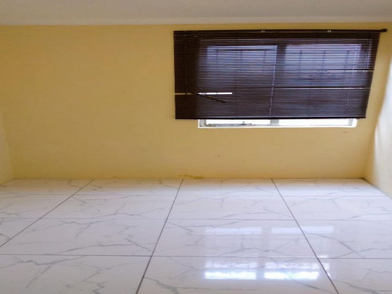 An empty bedroom featuring white marble-look floor tiles and a window fitted with dark venetian blinds.