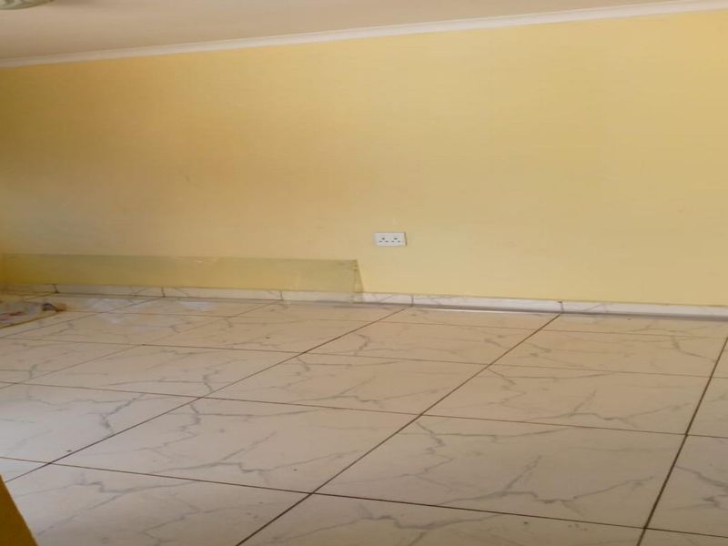 An empty living area featuring light-colored floor tiles and yellow painted walls, suitable for renovation or staging.