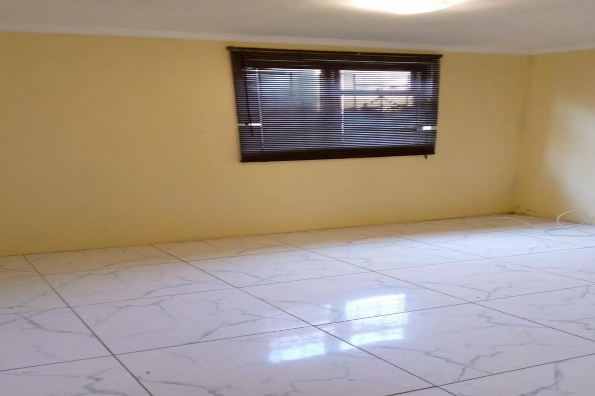 An empty bedroom featuring white marble-look tiled flooring and a window fitted with dark venetian blinds.