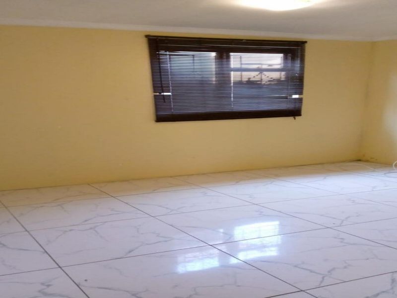 An empty bedroom featuring white marble-look tiled flooring and a window fitted with dark venetian blinds.
