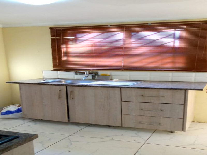 A functional kitchen area featuring built-in cabinetry, a stainless steel sink with mixer tap, tiled backsplash, and tiled flooring.
