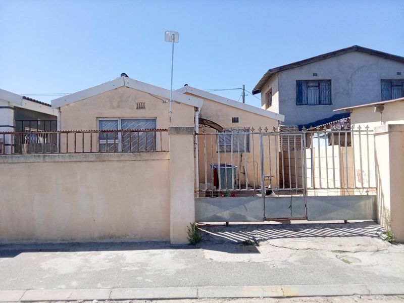 Front elevation of a single-story house featuring a perimeter wall, metal security gate, and tiled roof, showing signs of exterior wear.