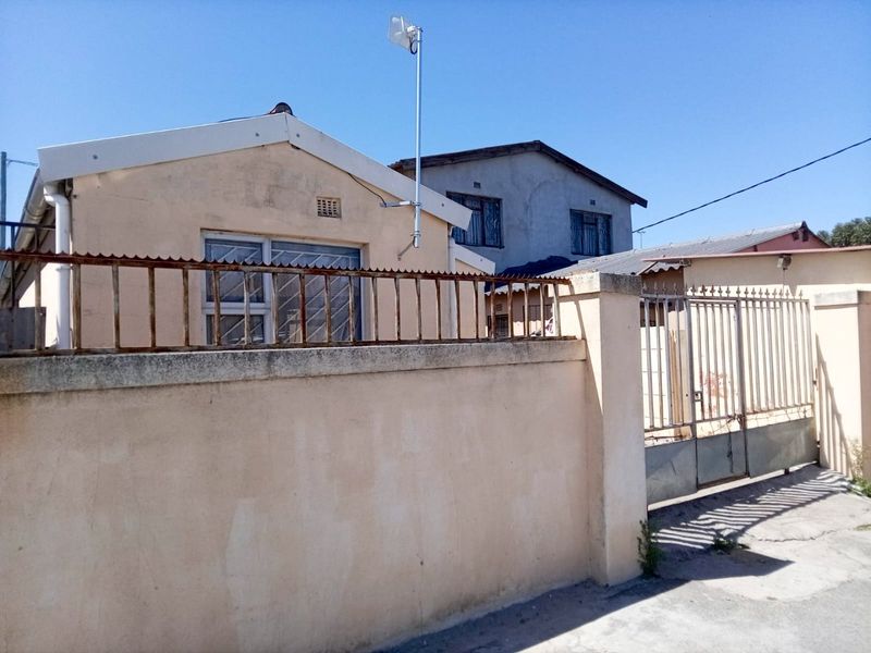 Front exterior view of the property featuring a perimeter wall, metal security gate, and security bars on the windows.