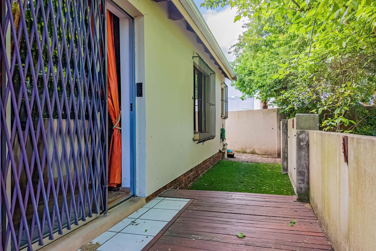 Rear exterior view featuring timber decking, a security gate, and a side garden area with boundary walling.