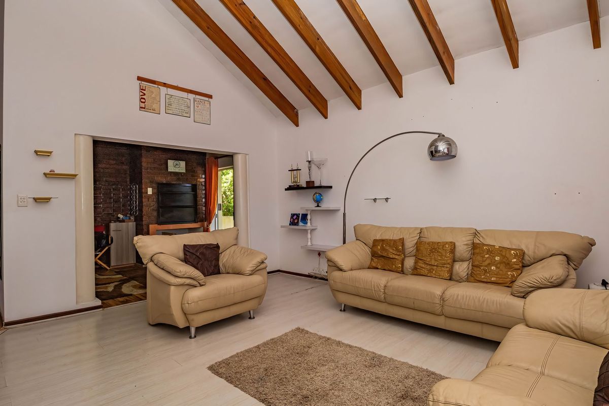 Spacious living room featuring a vaulted ceiling with exposed timber beams, laminate flooring, and an adjacent brick fireplace area.