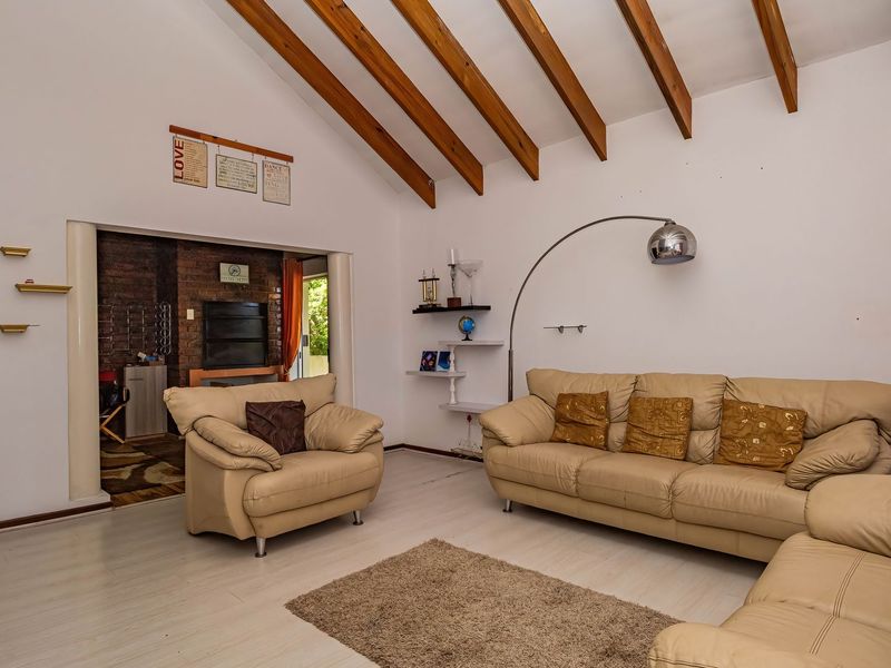 Spacious living room featuring a vaulted ceiling with exposed timber beams, laminate flooring, and an adjacent brick fireplace area.