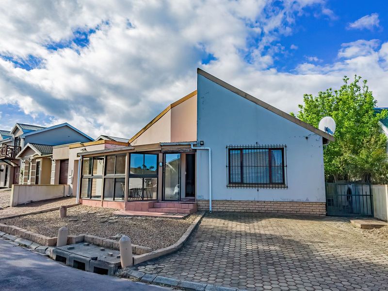 Front elevation of a residential house featuring a paved driveway, enclosed patio area, and security window bars.